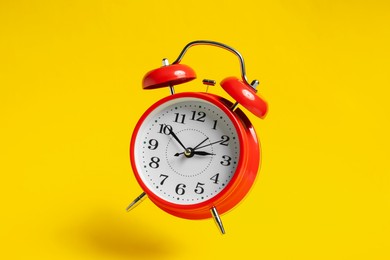Photo of Red alarm clock in air on yellow background