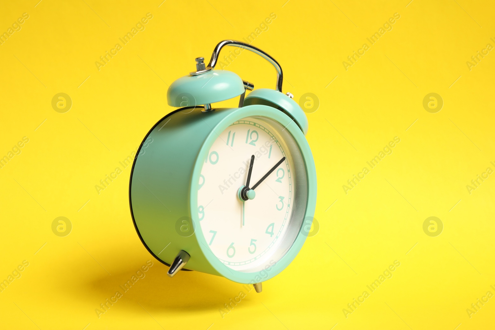 Photo of Turquoise alarm clock in air on yellow background