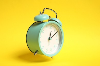 Photo of Turquoise alarm clock in air on yellow background