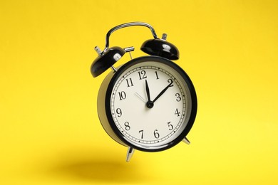 Photo of Black alarm clock in air on yellow background