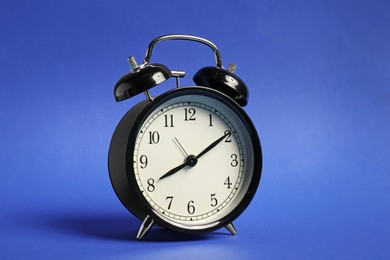 Photo of One black alarm clock on blue background
