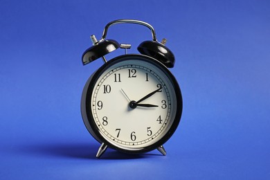 Photo of One black alarm clock on blue background