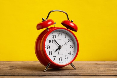 Photo of One red alarm clock on wooden table against yellow background