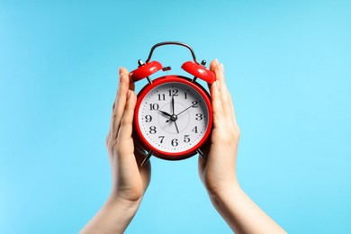 Photo of Woman with red alarm clock on light blue background, closeup
