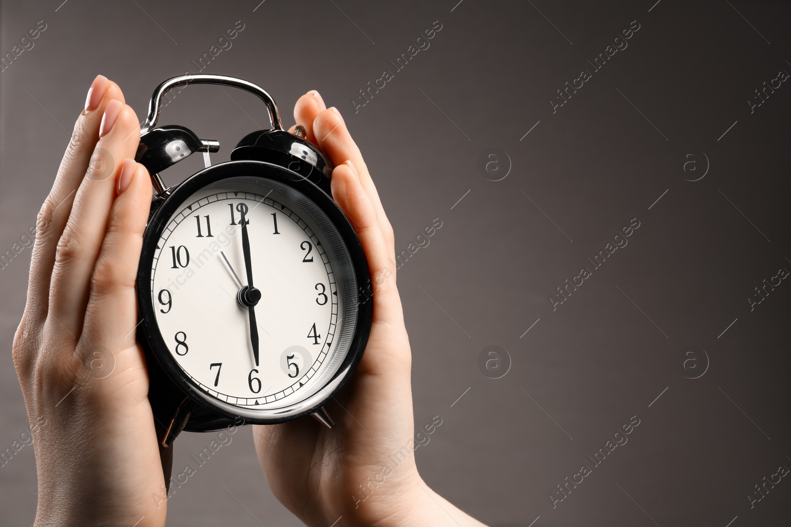 Photo of Woman with black alarm clock on grey background, closeup. Space for text