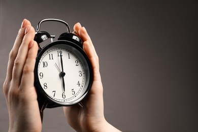 Photo of Woman with black alarm clock on grey background, closeup. Space for text