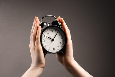 Photo of Woman with black alarm clock on grey background, closeup