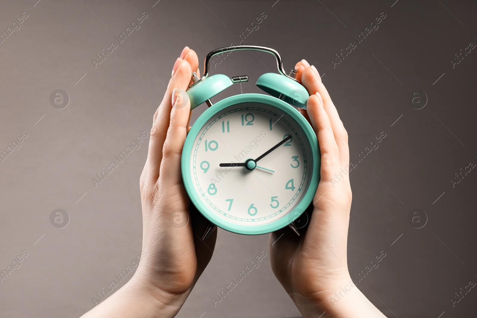 Photo of Woman with turquoise alarm clock on grey background, closeup