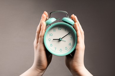 Photo of Woman with turquoise alarm clock on grey background, closeup