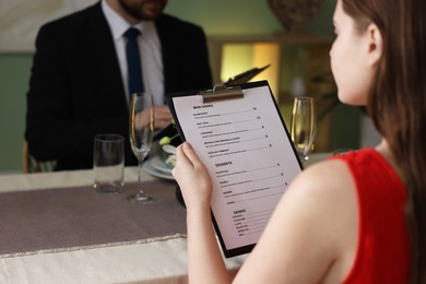 Photo of Couple choosing dishes from menu at table in restaurant, closeup