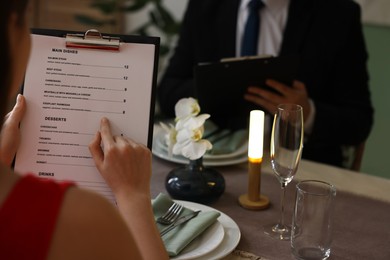 Photo of Couple choosing dishes from menu at table in restaurant, closeup