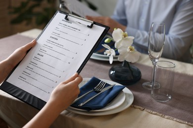 Photo of Couple choosing dishes from menu at table in restaurant, closeup