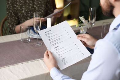 Couple choosing dishes from menu at table in restaurant, closeup