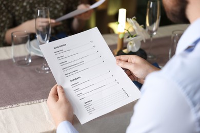 Photo of Couple choosing dishes from menu at table in restaurant, closeup