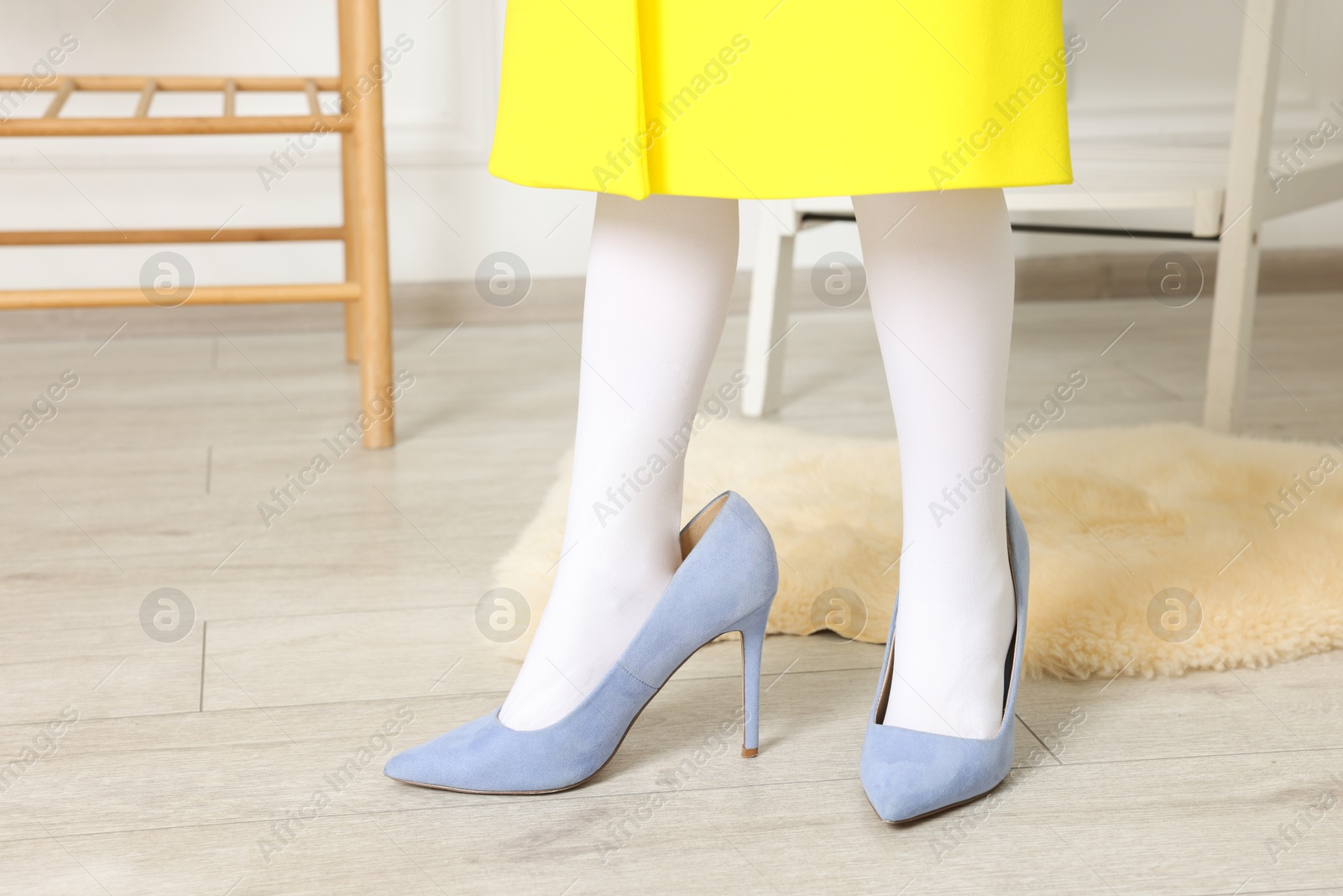 Photo of Little girl wearing oversized high heeled shoes indoors, closeup