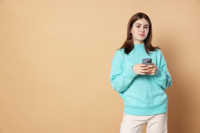 Photo of Portrait of beautiful teenage girl with smartphone on beige background. Space for text