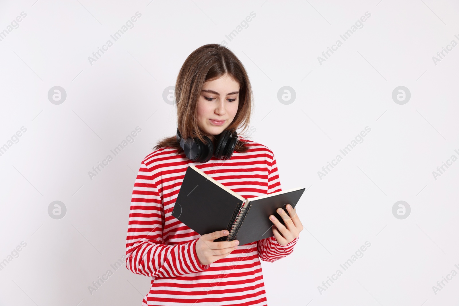 Photo of Portrait of teenage girl with headphones reading book on light background