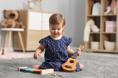 Photo of Cute little girl playing with toy guitar on floor at home