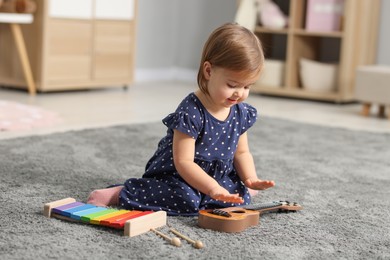 Photo of Cute little girl playing with toy guitar on floor at home