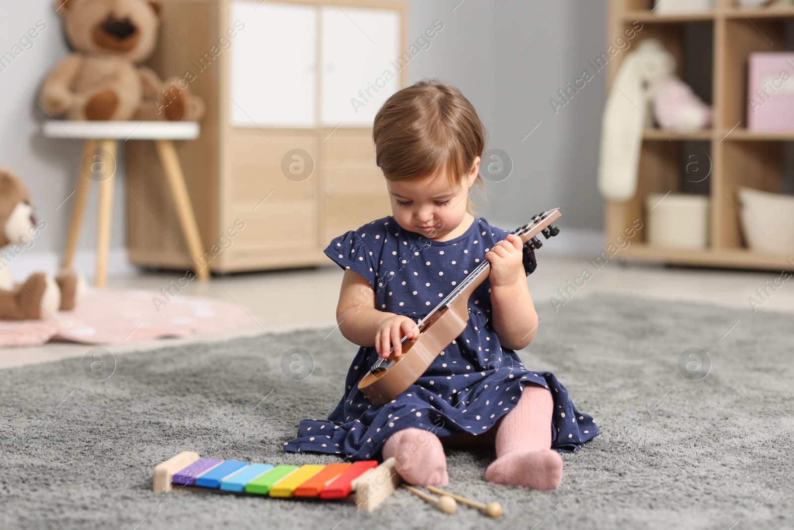 Photo of Cute little girl playing with toy guitar on floor at home