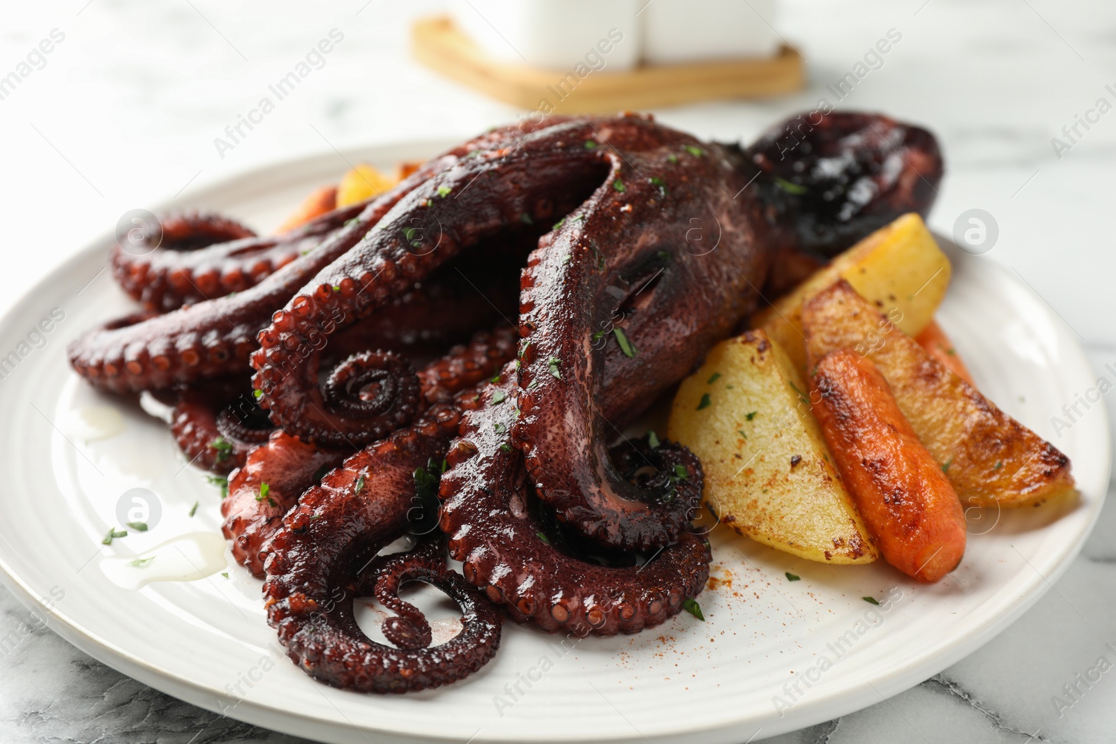 Photo of Roasted octopus with vegetables on white marble table, closeup