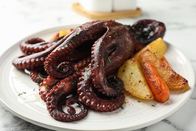 Photo of Roasted octopus with vegetables on white marble table, closeup