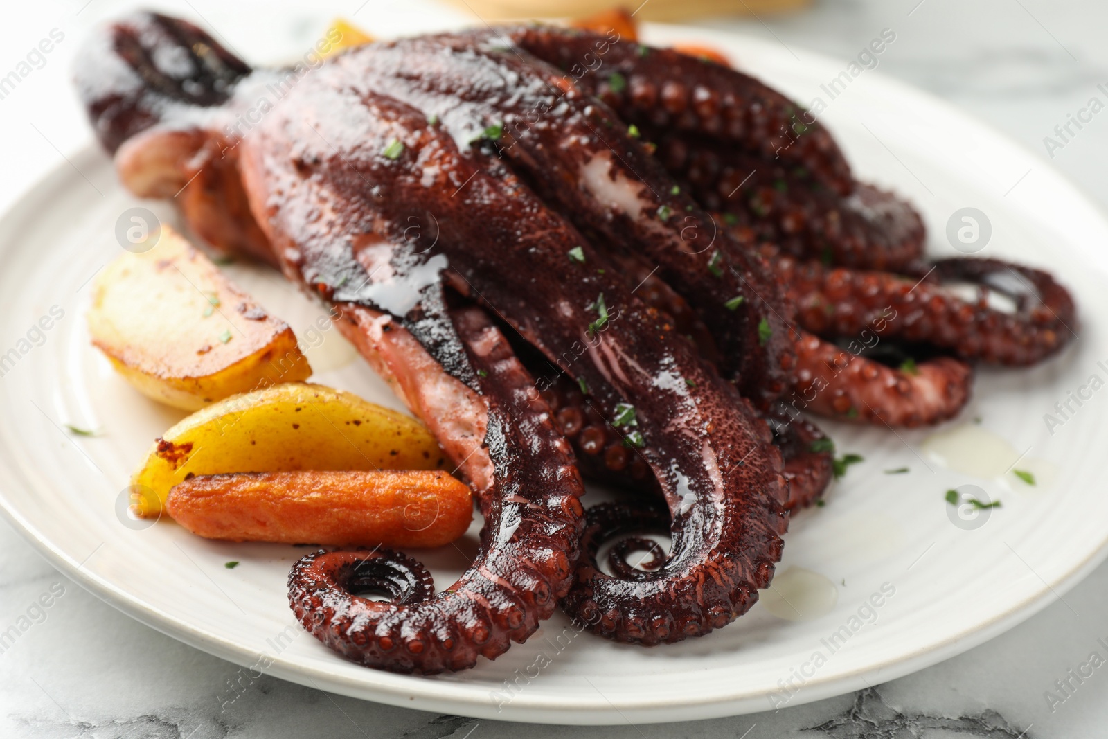 Photo of Roasted octopus with vegetables on white marble table, closeup