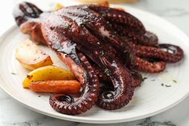 Roasted octopus with vegetables on white marble table, closeup