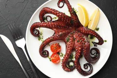 Photo of Fried octopus with herb sauce, lemon and tomatoes on dark textured table, flat lay