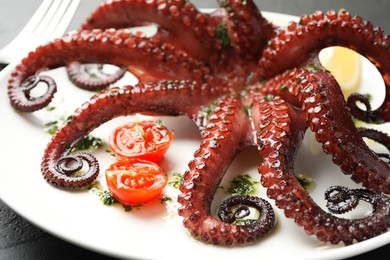 Fried octopus with herb sauce and tomatoes on dark textured table, closeup