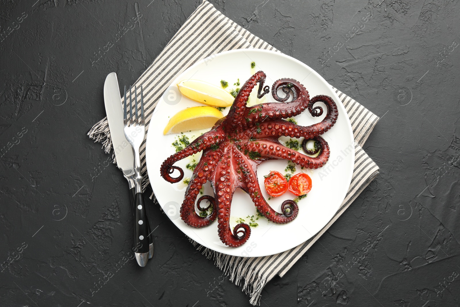 Photo of Fried octopus with herb sauce, lemon and tomatoes served on dark textured table, flat lay