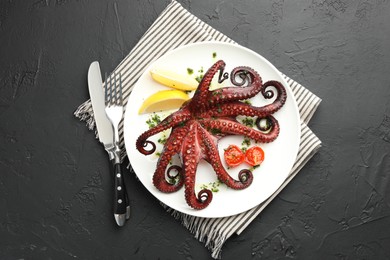 Photo of Fried octopus with herb sauce, lemon and tomatoes served on dark textured table, flat lay