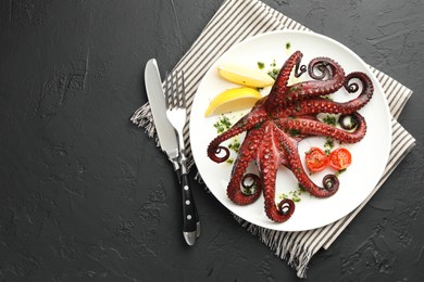 Photo of Fried octopus with herb sauce, lemon and tomatoes served on dark textured table, flat lay. Space for text