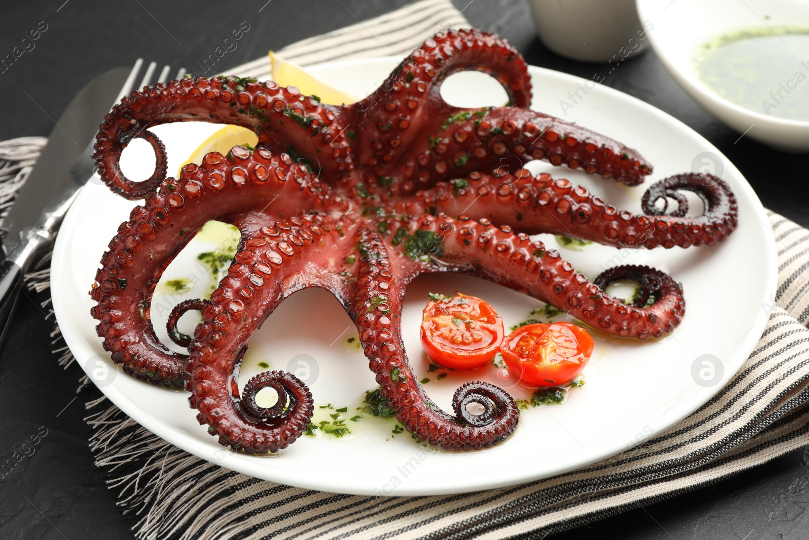 Photo of Fried octopus with herb sauce and tomatoes on grey table, closeup