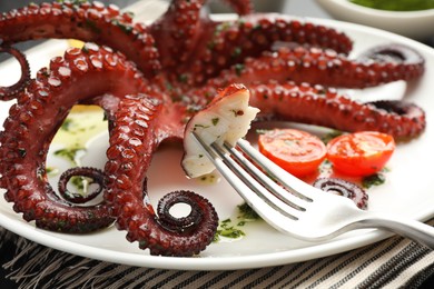 Eating tasty fried octopus with herb sauce at table, closeup