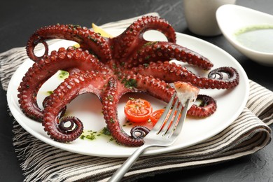 Photo of Eating tasty fried octopus with herb sauce at dark textured table, closeup