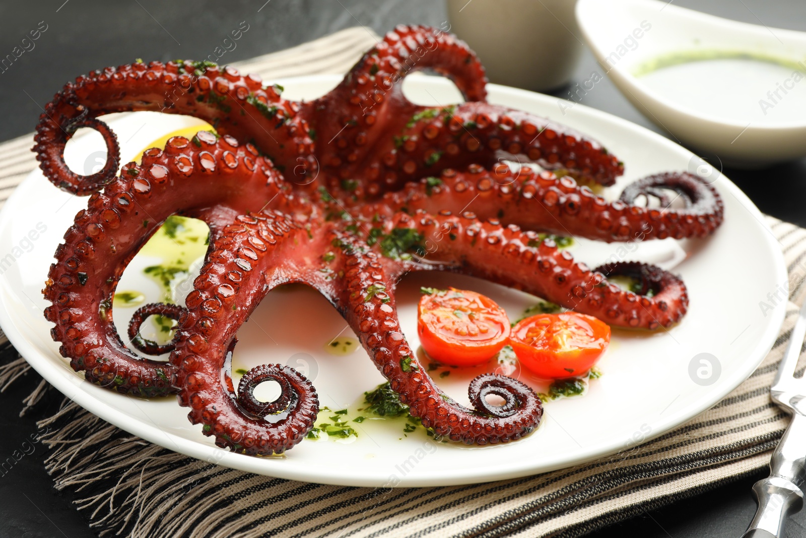 Fried octopus with herb sauce and tomatoes on grey table, closeup Photo of Fried octopus with herb sauce and tomatoes on grey table, closeup