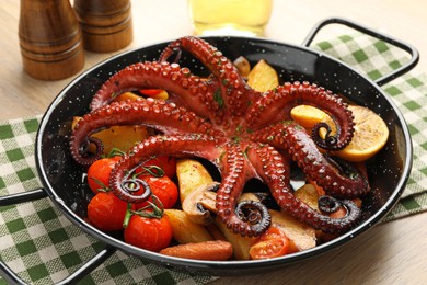 Photo of Fried octopus with mushrooms, lemon and vegetables in pan on wooden table, closeup