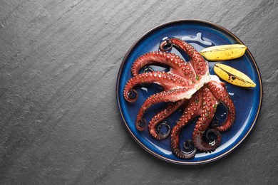 Fried octopus with herb sauce and lemon on grey textured table, top view. Space for text