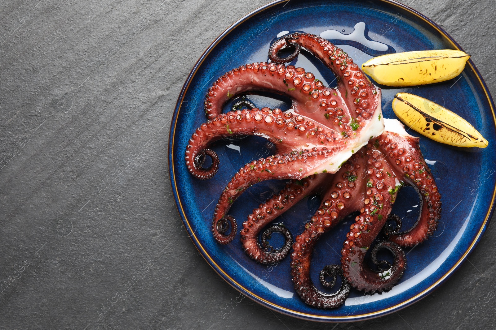 Photo of Fried octopus with herb sauce and lemon on grey textured table, top view. Space for text