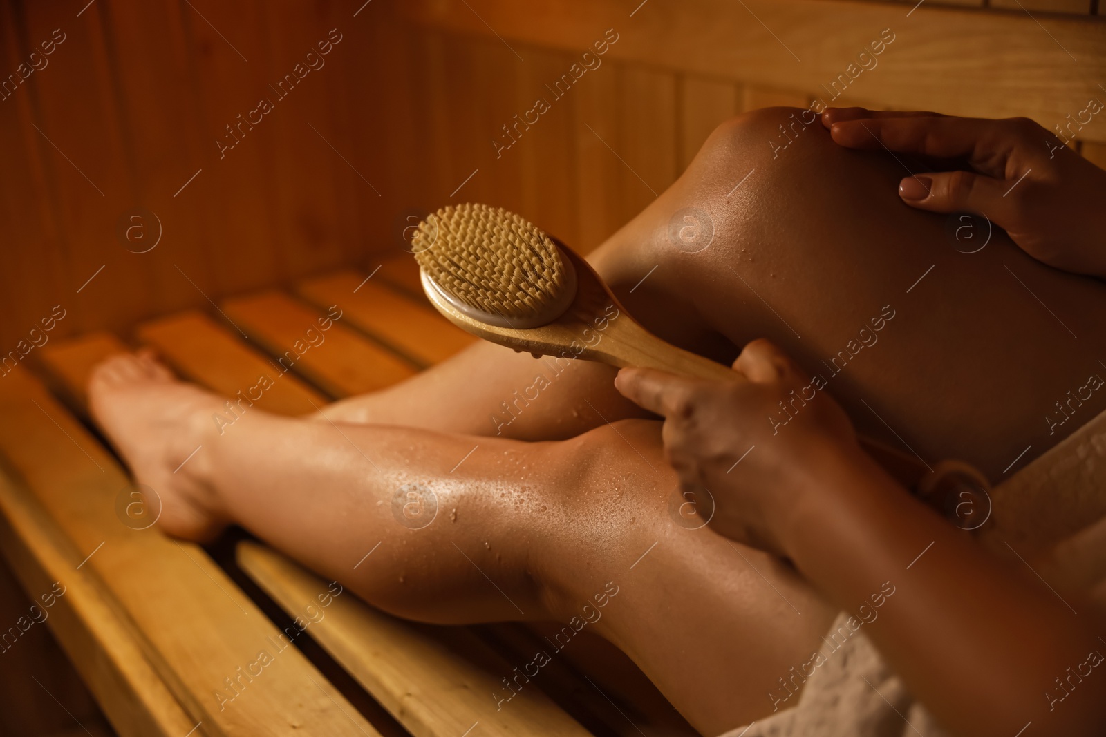 Photo of Woman with massage brush on bench in sauna, closeup