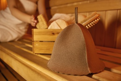 Photo of Woman with bath accessories and felt wool hat on wooden bench in sauna, selective focus