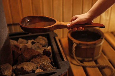 Photo of Woman pouring water on stones in sauna, closeup