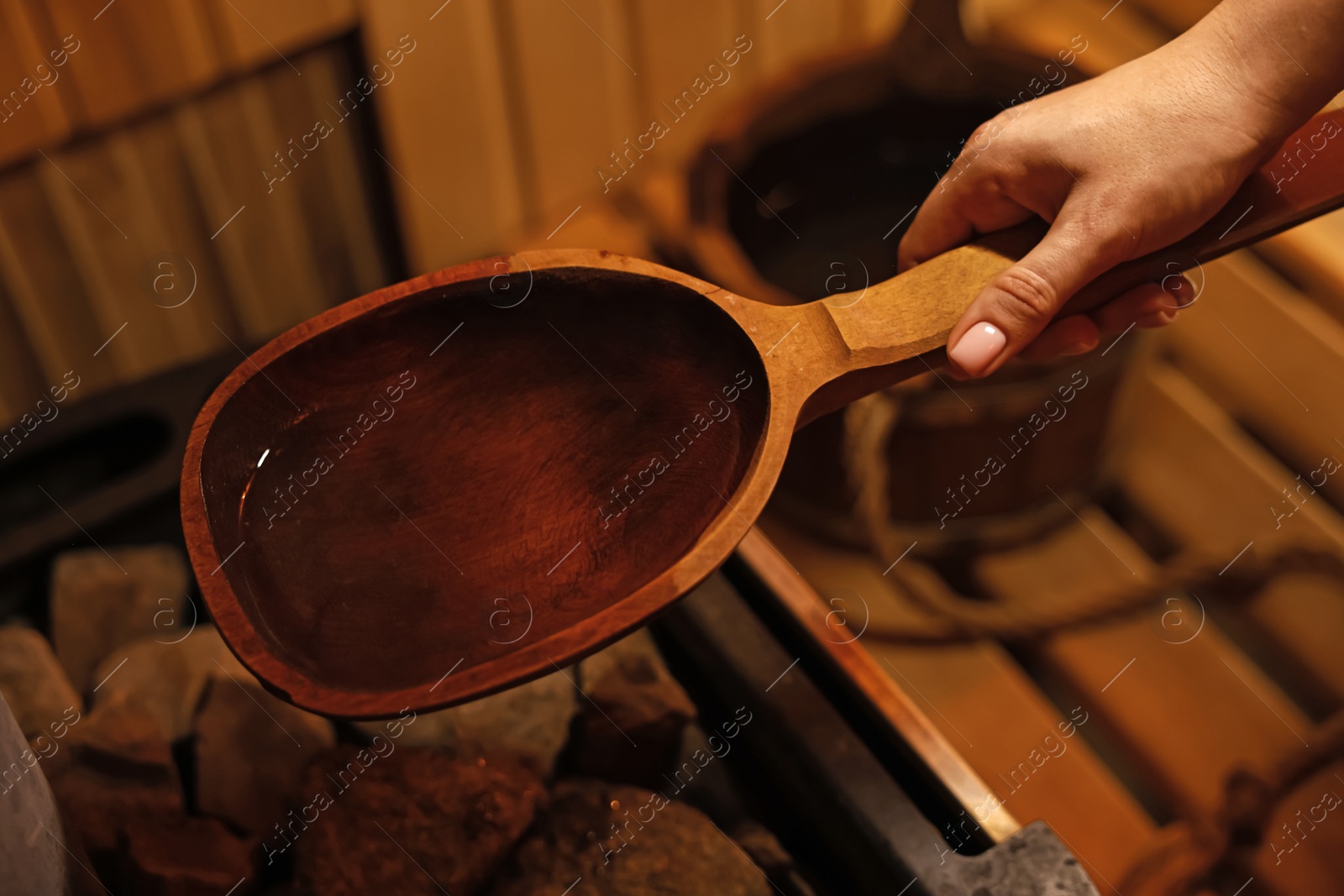 Photo of Woman pouring water on stones in sauna, closeup