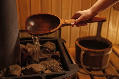 Photo of Woman pouring water on stones in sauna, closeup