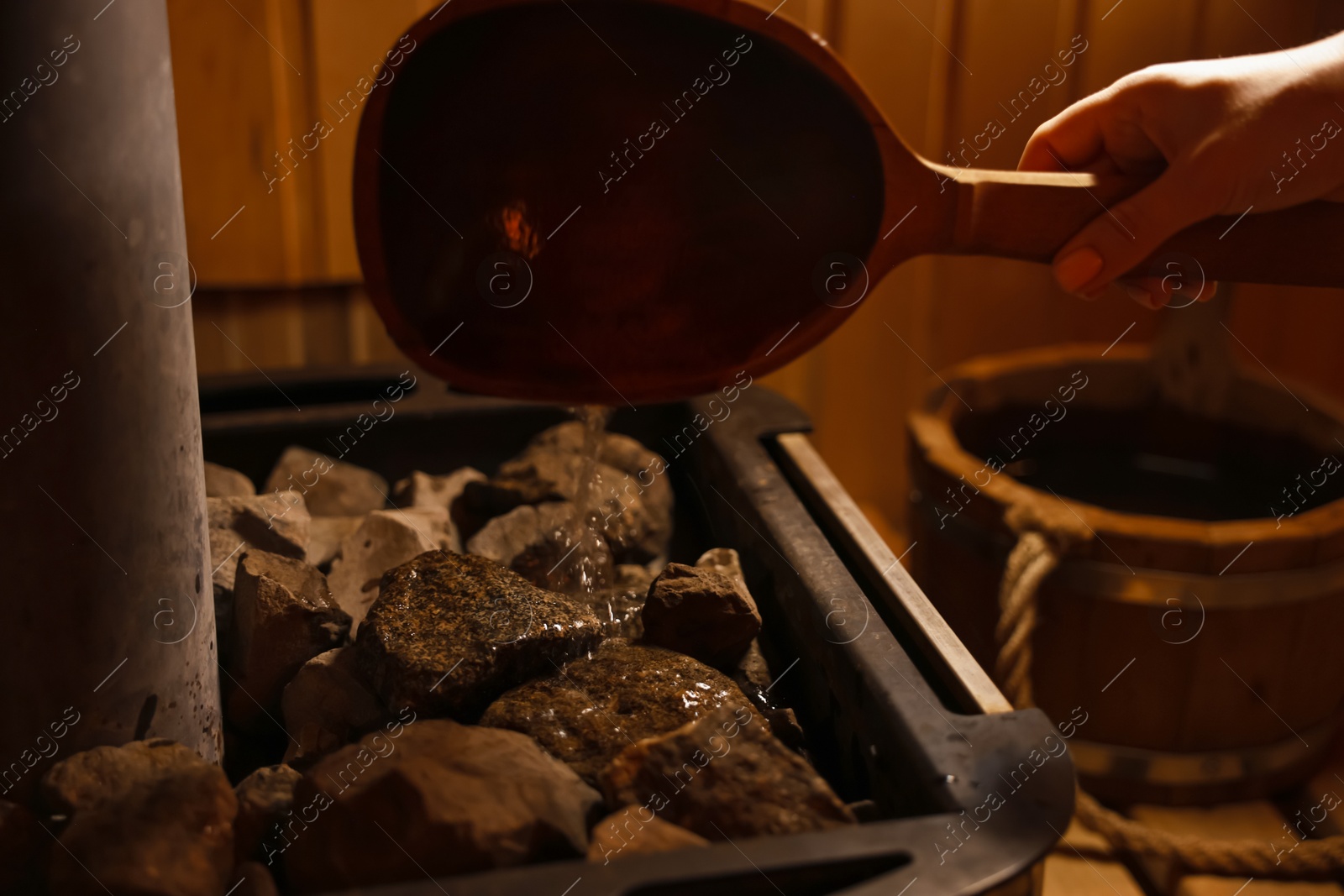 Photo of Woman pouring water on stones in sauna, closeup