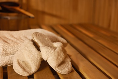 Photo of Towels and slippers on wooden bench in sauna. Space for text