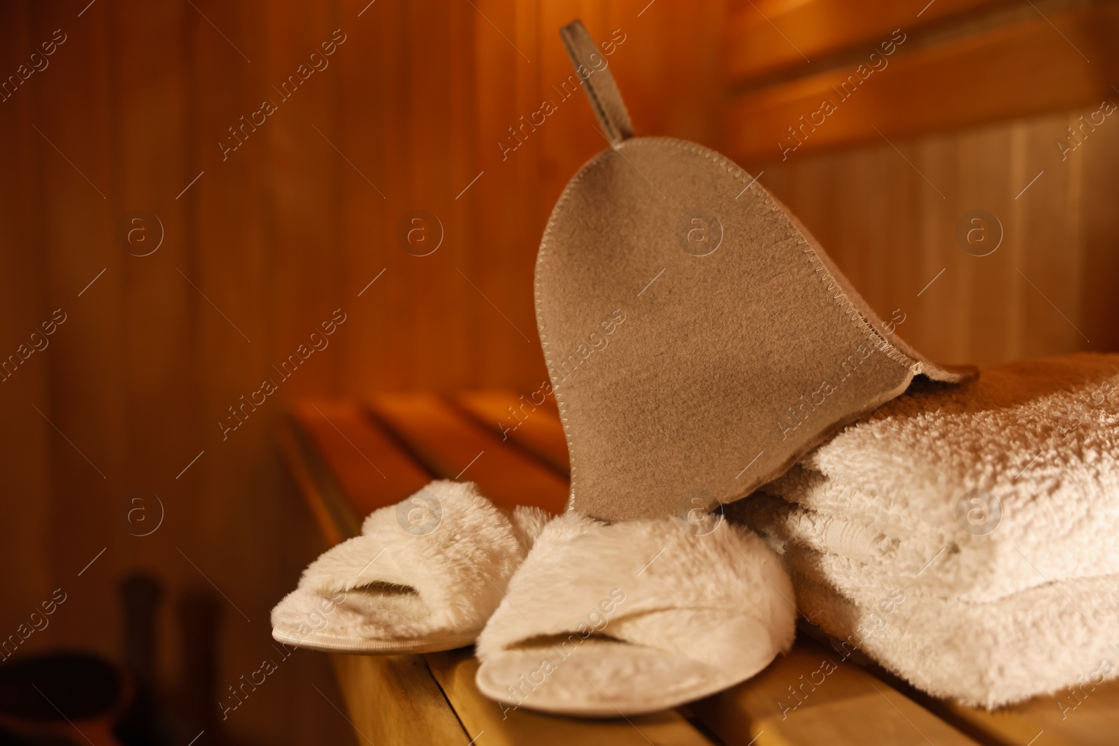 Photo of Felt wool hat, towels and slippers on wooden bench in sauna. Space for text