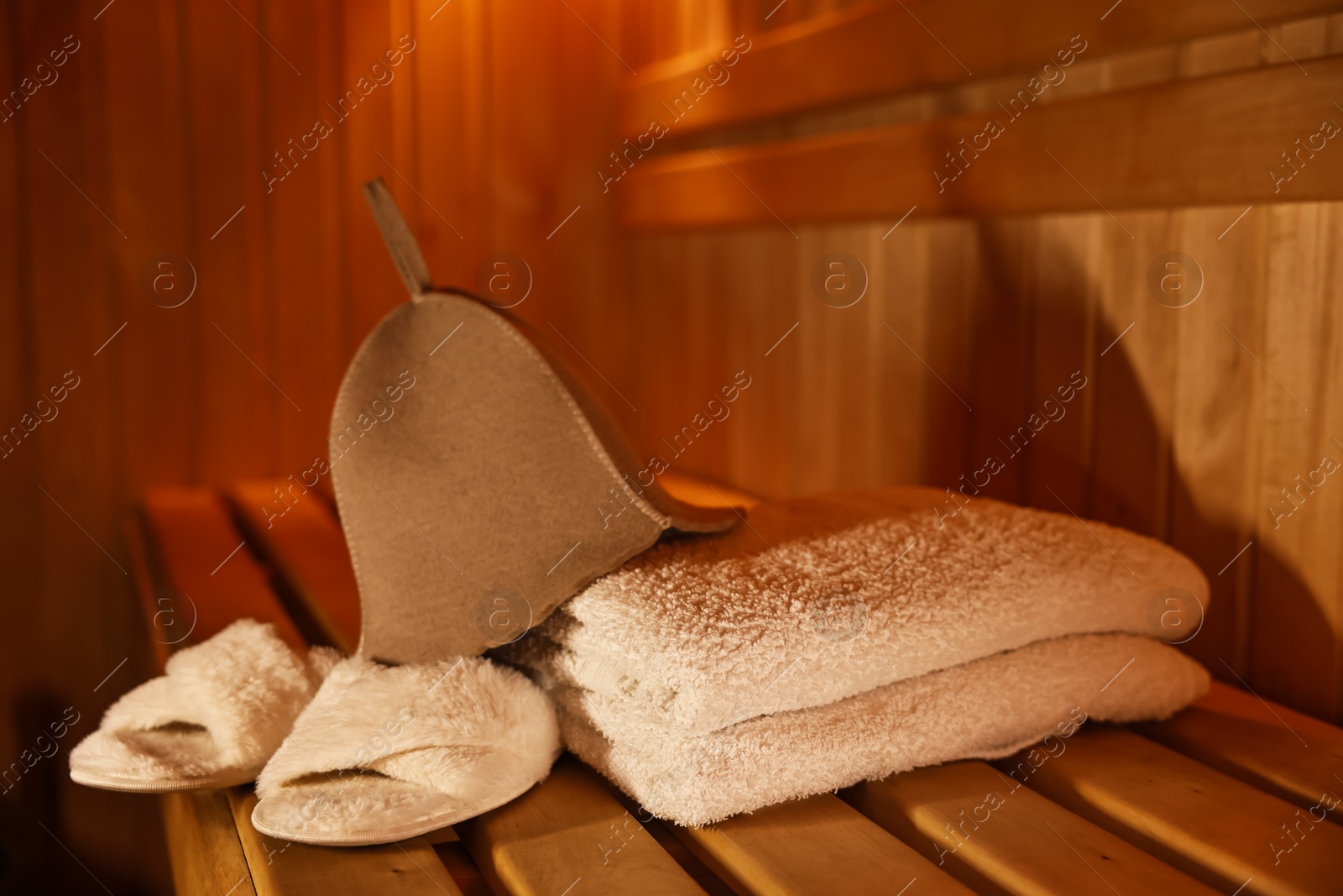 Photo of Felt wool hat, towels and slippers on wooden bench in sauna