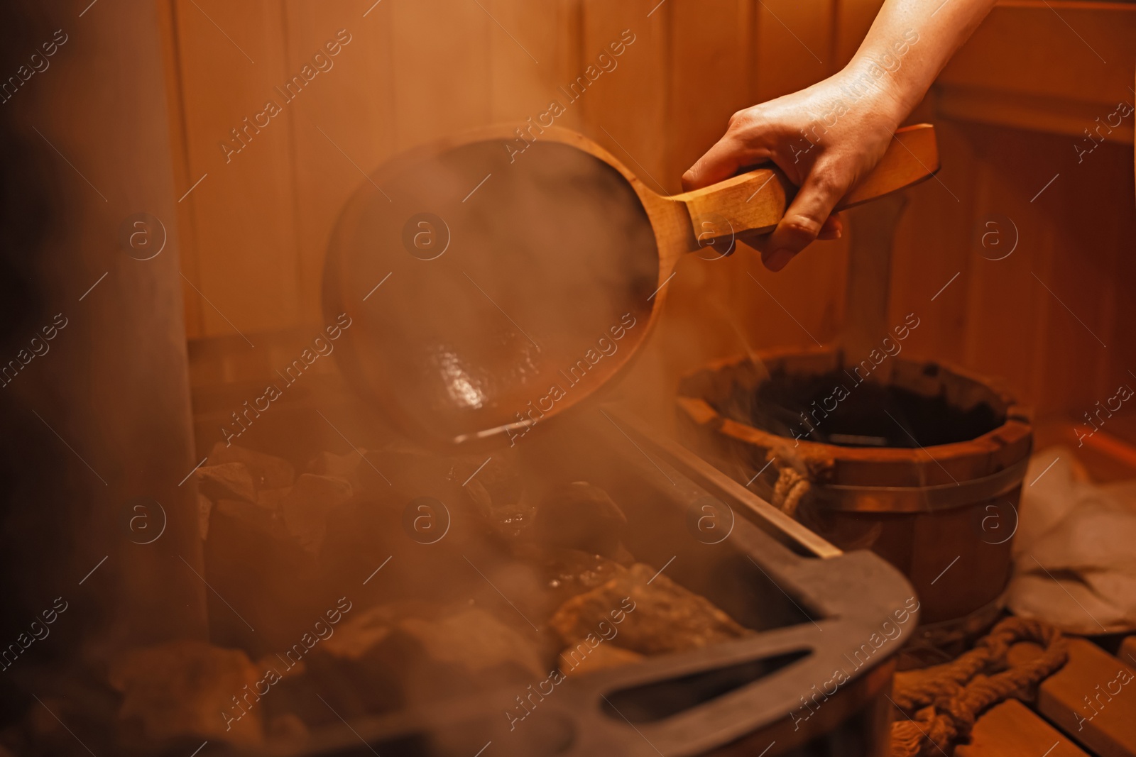 Photo of Woman pouring water on stones in sauna, closeup